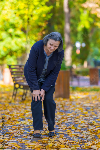 Senior woman having knee pain walking in park photo