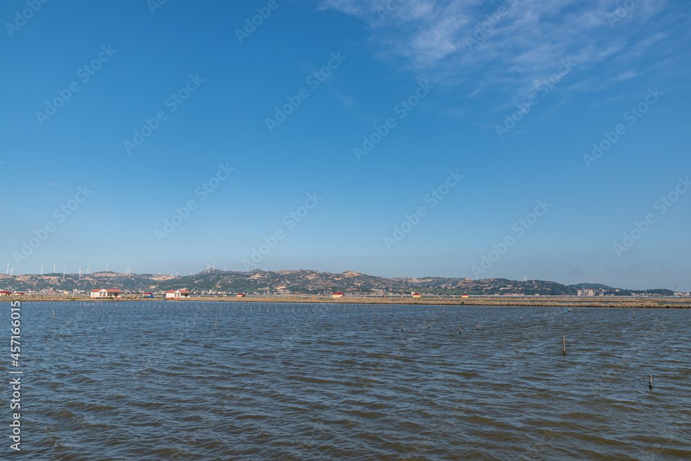 The coastline under the blue sky, opposite the sea are mountains and wind power