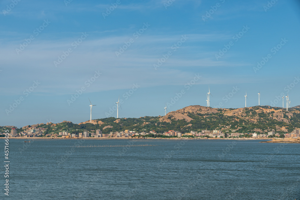 The coastline under the blue sky, opposite the sea are mountains and wind power