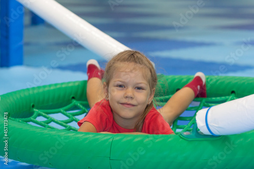 Caucasian little girl of five years old lying on round swing looking at camera in play center