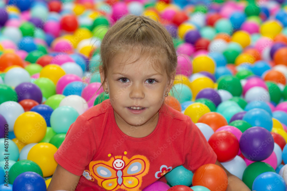 Obraz premium Caucasian little girl of five years old looking at camera among multicolor balls in play center