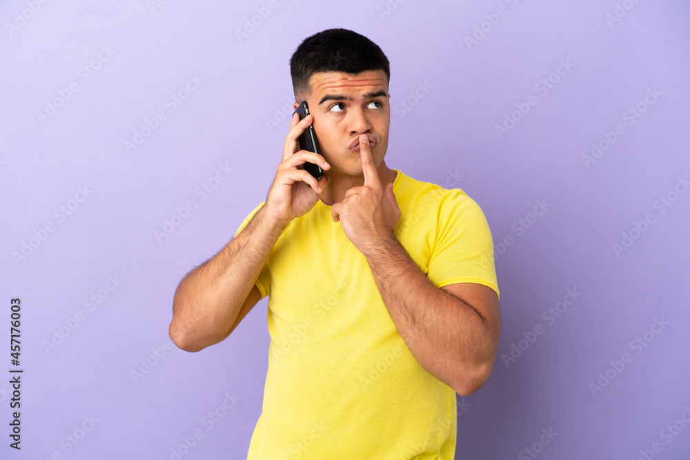 Young handsome man using mobile phone over isolated purple background having doubts while looking up Young handsome man using mobile phone over isolated purple background having doubts while looking up