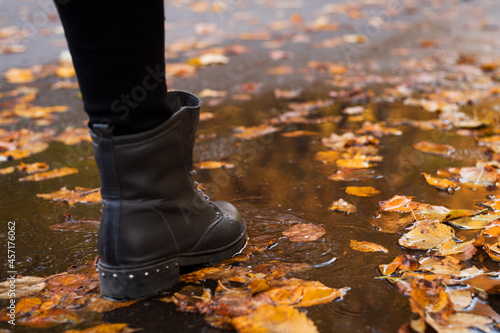 Colourful fall leaves in pond lake water, and boots of a passerby going through the water puddle. Rainy autumn weather