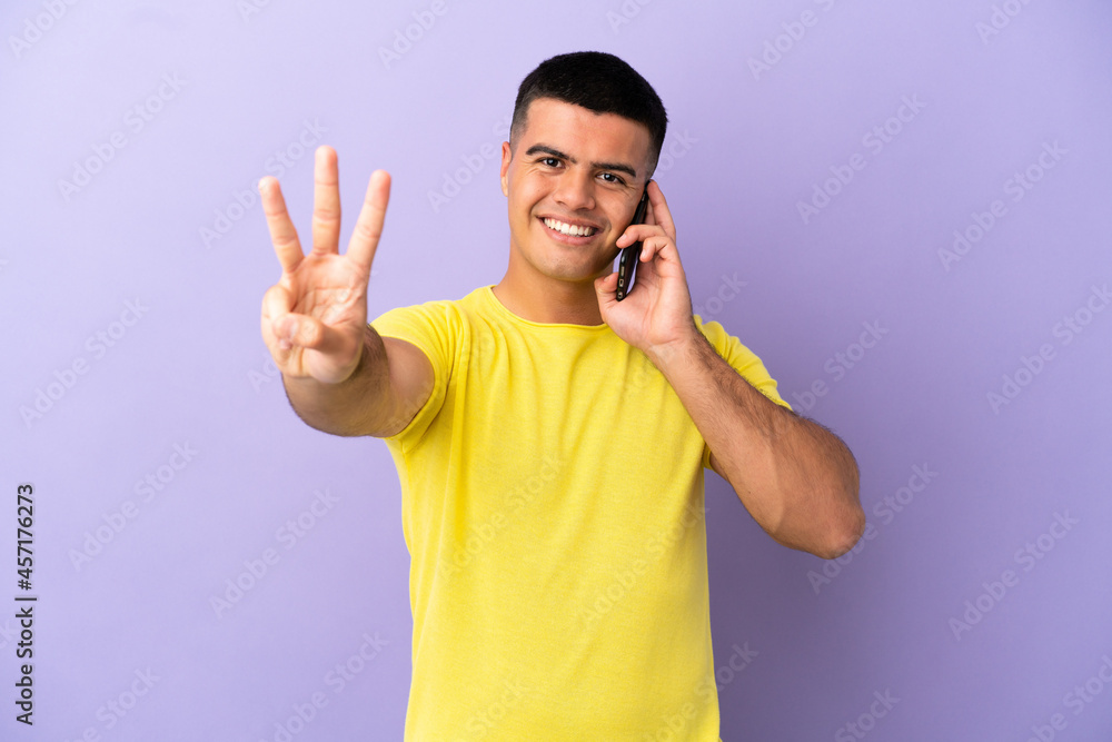 Fototapeta premium Young handsome man using mobile phone over isolated purple background happy and counting three with fingers