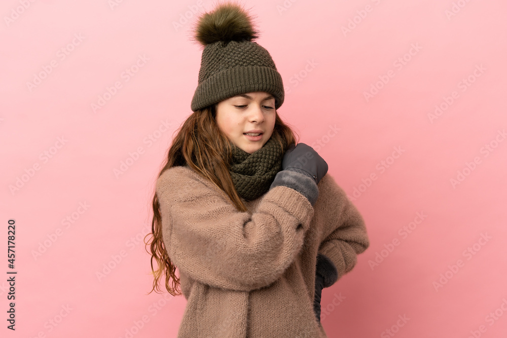 Little girl with winter hat isolated on pink background suffering from pain in shoulder for having made an effort