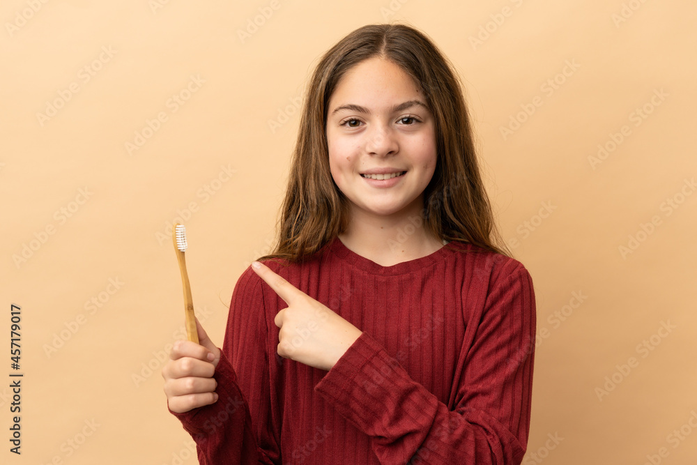 Little caucasian girl brushing her teeth isolated on beige background pointing to the side to present a product Little caucasian girl brushing her teeth isolated on beige background pointing to the side to present a product