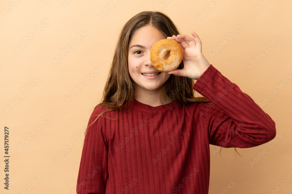 Little caucasian girl isolated on beige background holding donuts in eyes Little caucasian girl isolated on beige background holding donuts in eyes