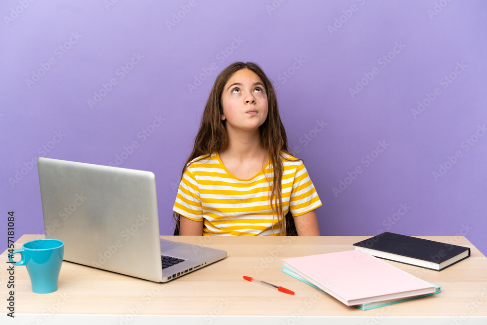 Naklejka premium Little student girl in a workplace with a laptop isolated on purple background and looking up