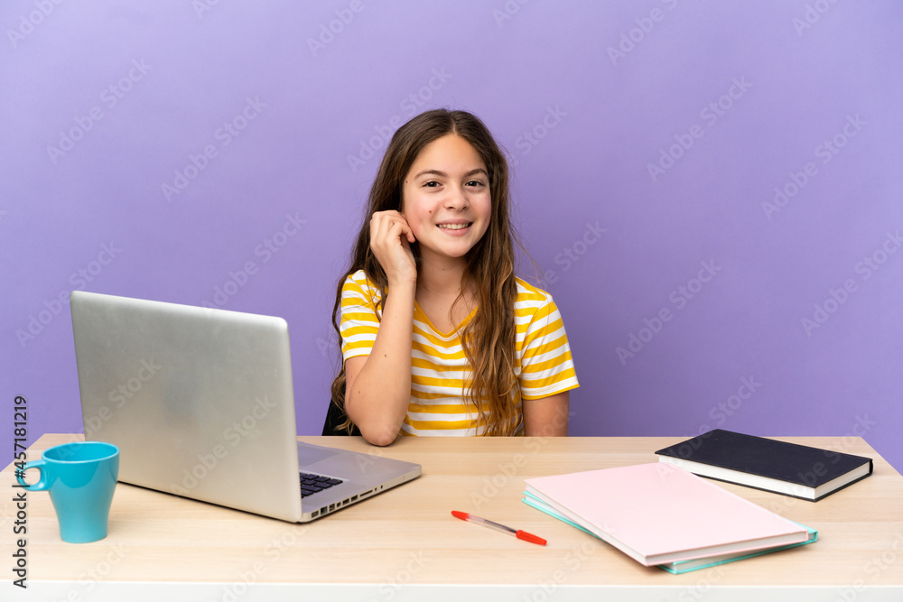 Little student girl in a workplace with a laptop isolated on purple background laughing Little student girl in a workplace with a laptop isolated on purple background laughing