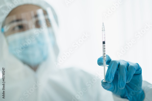 Unrecognizable specialist doctor in a medical PPE suit showing and looking at an injection needle.