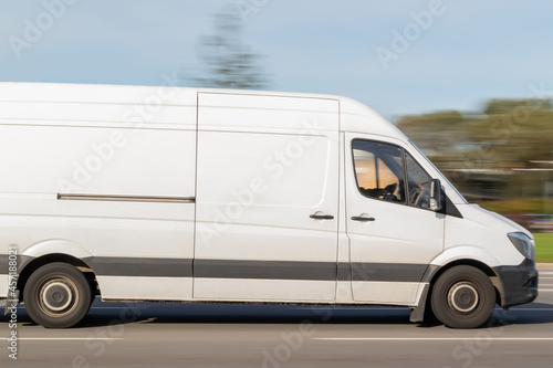 A white cargo bus is driving down the street. Freight transport by city with a van. Motion blur