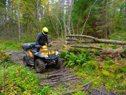 Man in a yellow helmet on an ATV. He rides his ATV through the forest. Off-road driving concept. ATV driver overcomes an obstacle on the road. Quad bike as a symbol of motorcycle racing