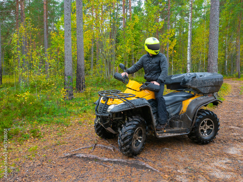 ATV racing concept. The ATV driver has stopped and looks around. Quad bike as a symbol of extreme sports Traveling through the forest on a quad bike. Man rides his own ATV. Extreme atv racing