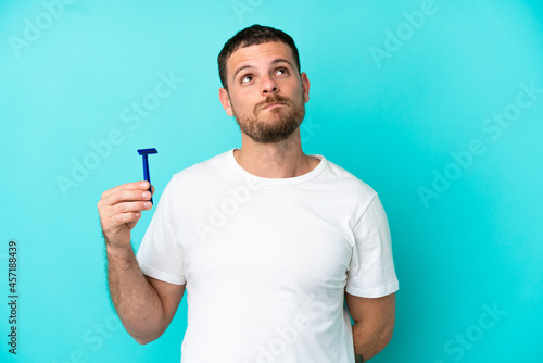 Brazilian man shaving his beard isolated on blue background and looking up