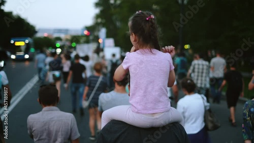 Revolt strike demonstration, young rebelling female child sits on shoulders. Daughter sitting on fathers shoulders. Family picketing activists in political rally crowd, peaceful resistance protest. photo