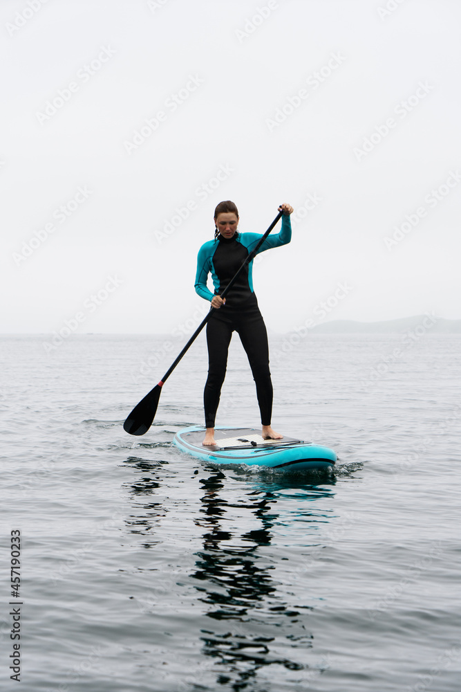 Fitness woman standing on surfboard enjoying supsurfing with paddle at endless sea water fog Fitness woman standing on surfboard enjoying supsurfing with paddle at endless sea water fog