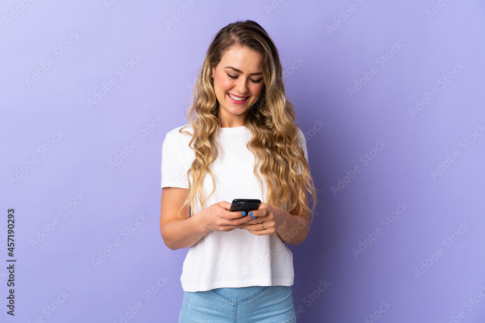 Young Brazilian woman isolated on purple background sending a message with the mobile Young Brazilian woman isolated on purple background sending a message with the mobile