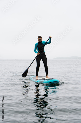 Fitness woman standing on surfboard enjoying supsurfing with paddle at endless sea water fog © Aboltin