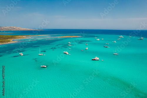 Aerial view of many yachts and sailboats in turquoise water in Mediterranean Sea next to Sardinia island, La Pelosa beach