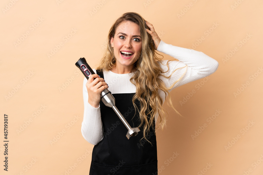 Young brazilian woman using hand blender isolated on beige background with surprise expression Young brazilian woman using hand blender isolated on beige background with surprise expression