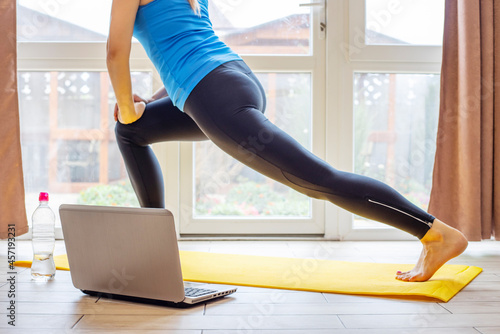 Beautiful young woman in sportswear doing sport exercises on yoga mat at home. Fitness training online with a laptop. Healthy lifestyle concept