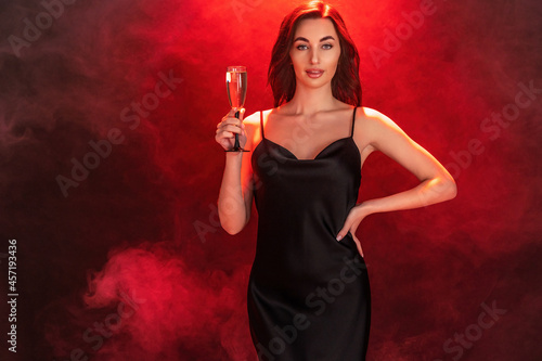 Beautiful young brunette woman in black dress holds glass of champagne. Party time. Holiday concept