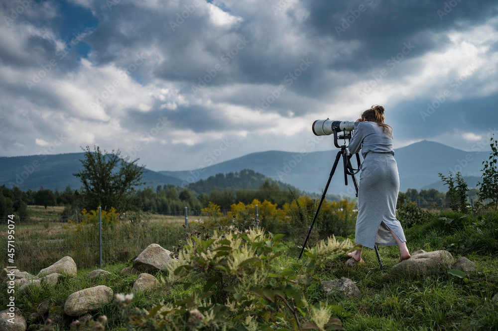 Female photographer taking a picture outdoors with a camera with large telephoto lens, mountains in the background.