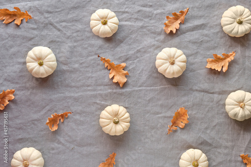 Autumn background with natural pumpkins and dry oak leaves. Flat lay, top view on grey uncolored linen textile. Geometric Fall background with simple, minimal seasonal decor.