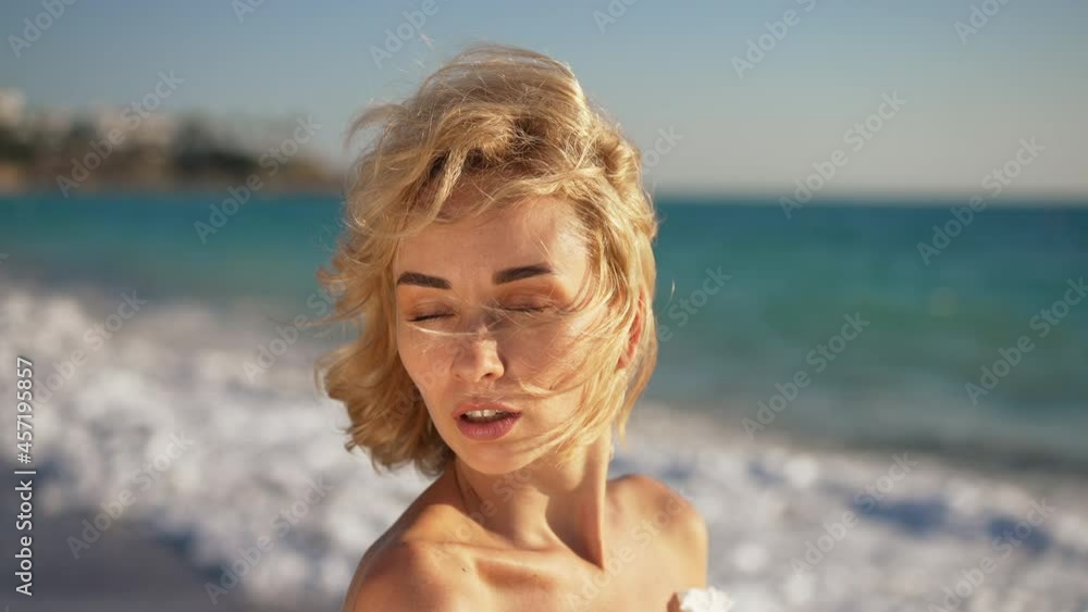 Close-up portrait of gorgeous sensual young woman posing in sunshine at picturesque Mediterranean sea beach with foamy blue waves rolling in slow motion. Live camera moves around confident tourist Close-up portrait of gorgeous sensual young woman posing in sunshine at picturesque Mediterranean sea beach with foamy blue waves rolling in slow motion. Live camera moves around confident tourist