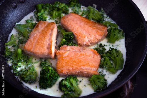 Frying pan with fresh delicious dinner. Piece of salmon fish with broccoli pieces in garlic cream sauce. Easy recipe of restaurant menu dish. Ideas for everyday cooking of diet and healthy nutrition.