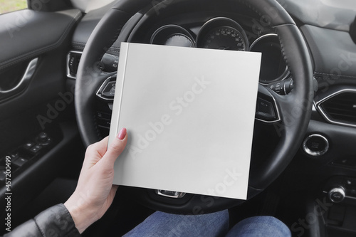Square book in the girl's hand on car steering wheel mockup photo