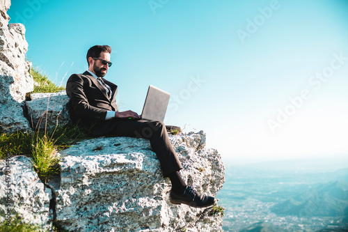 Businessman sitting with laptop on a rock.