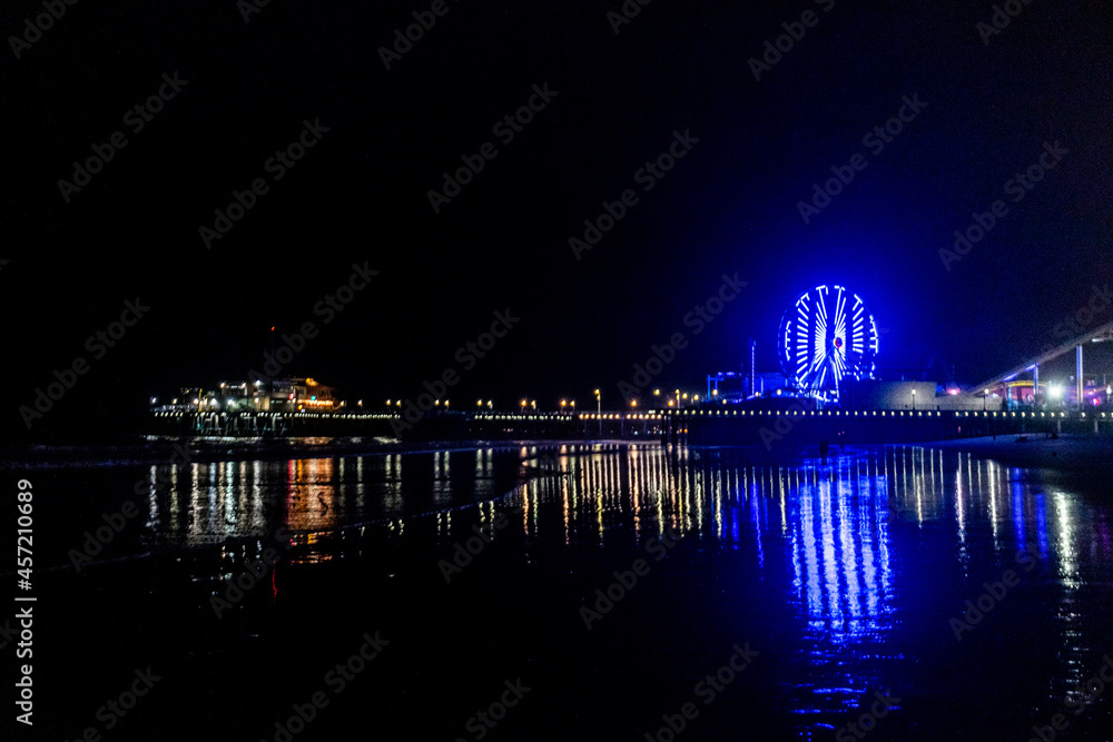 Fototapeta premium The lights of the Santa Monica Pier, the Ferris wheel and the Rollercoaster reflected in the water of the Pacific Ocean on Santa Monica Beach.
