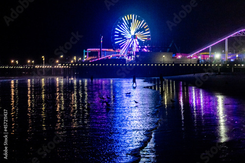 The lights of the Santa Monica Pier, the Ferris wheel and the Rollercoaster reflected in the water of the Pacific Ocean on Santa Monica Beach.