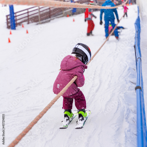 Ski training slope. Young child on ski going up on slope with surface baby lift