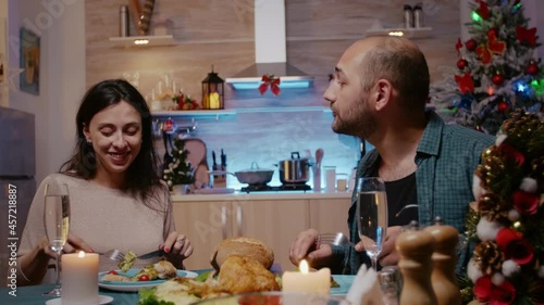 Man and woman celebrating christmas with festive dinner, enjoying traitional meal and drinking alcohol. Couple eating chicken and having glasses of champagne while chatting on holiday photo
