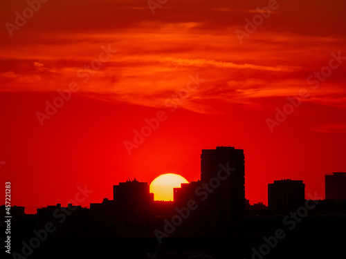Burgundy sunset over the city. The bright sun sets between high-rise buildings. Cityscape at sunset. Red sunset and black silhouette of the city. Copy space
