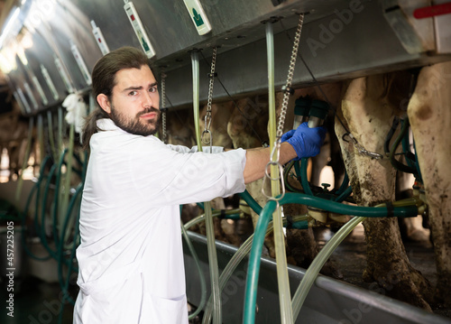 Farm dairymaid young man in bathrobe working with automatical cow milking machines