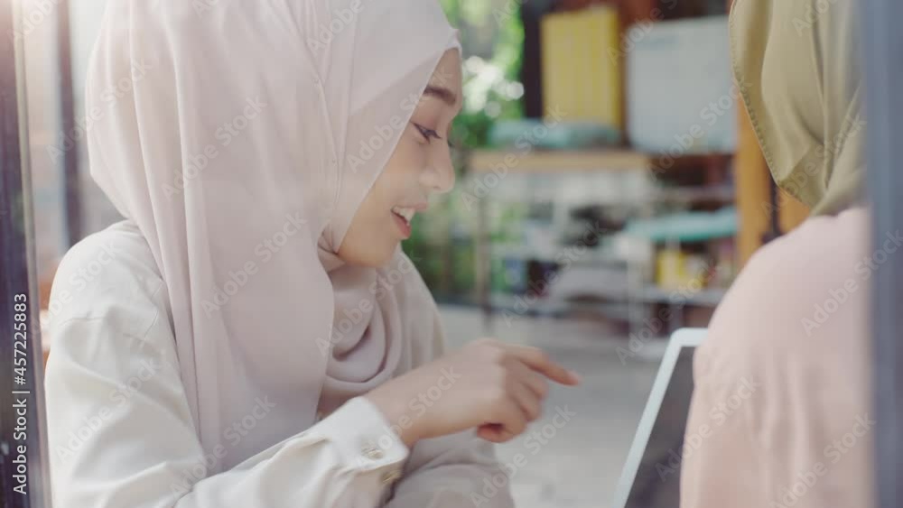 Young beautiful Asian Muslim women sitting by the window enjoying a relaxing moment playing with mobile phone in the coffee shop on a bright sunny day Young beautiful Asian Muslim women sitting by the window enjoying a relaxing moment playing with mobile phone in the coffee shop on a bright sunny day