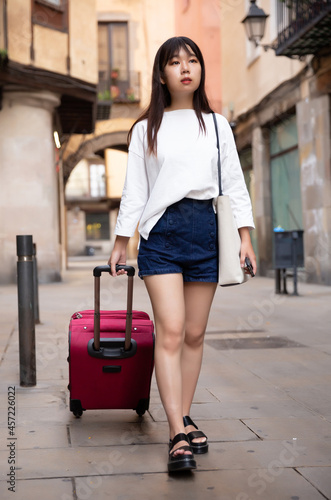 Happy young chinese tourist taking walk in city with the travel bag. High quality photo