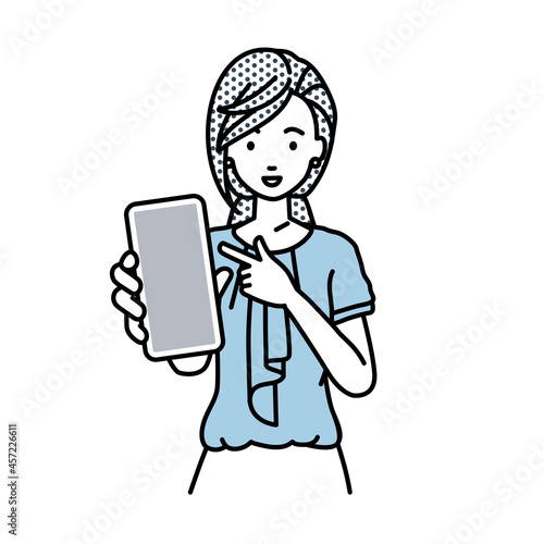 立ってスマートフォンを指差してこちらに向けて見せているオフィスカジュアルの女性