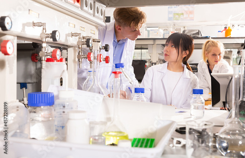 Chinese female student with male groupmate performing experiments in university chemistry laboratory, recording results in workbook