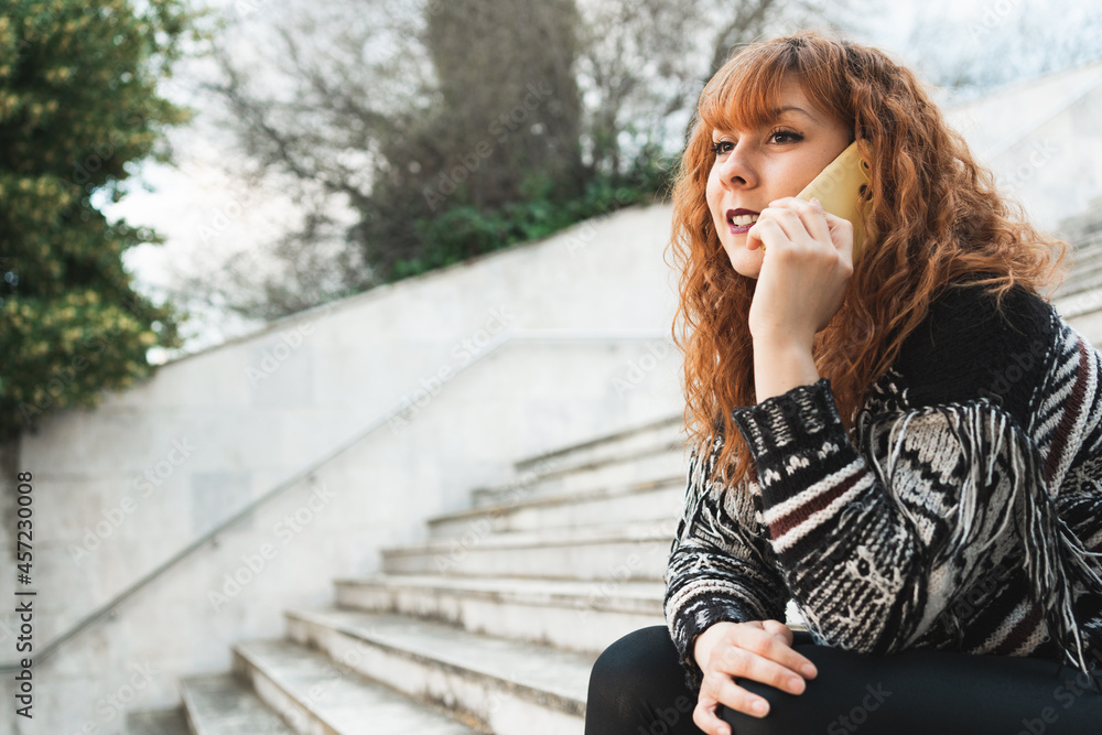 Young caucasian female talking on the phone sitting on the stair outside. copy space. Young caucasian female talking on the phone sitting on the stair outside. copy space.