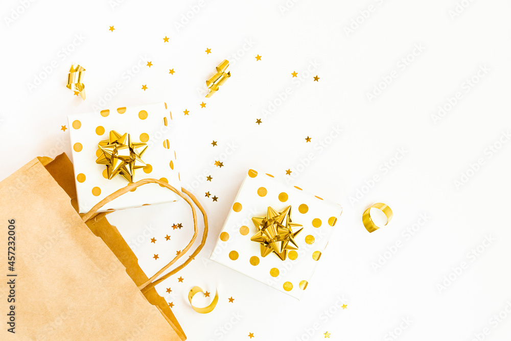 Top view of golden dotted gift boxes, a shopping bag and star shaped golden confetti on a white background. Copy space.