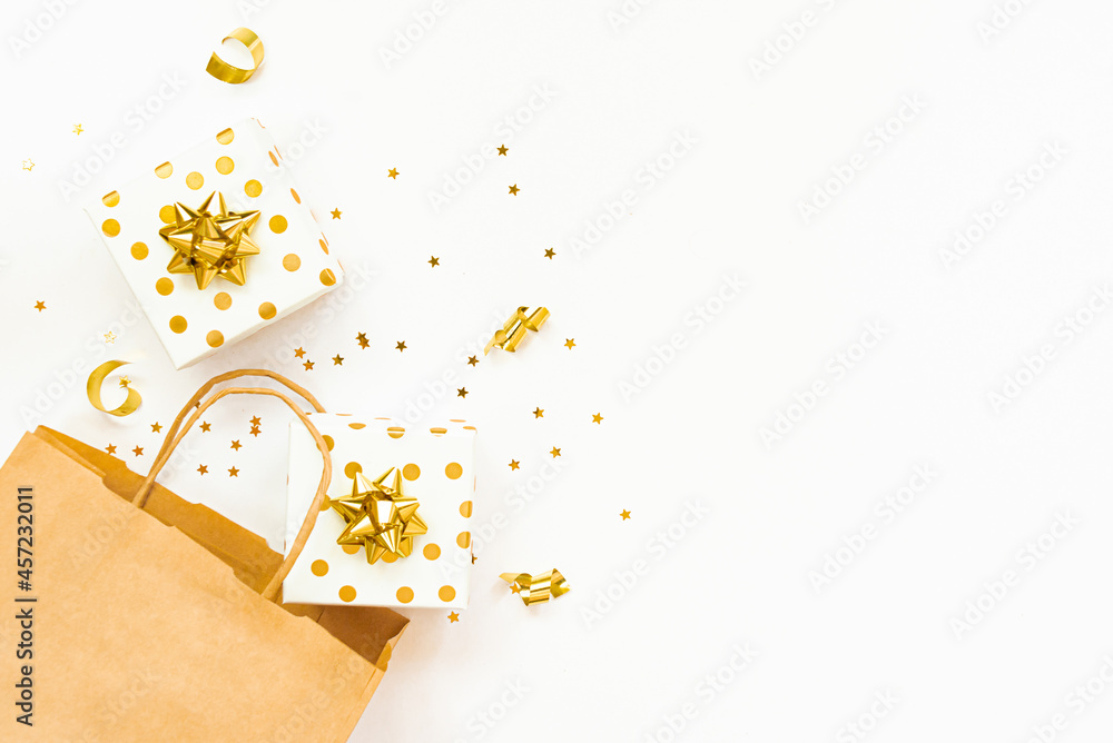 Top view of golden dotted gift boxes, a shopping bag and star shaped golden confetti on a white background. Copy space.