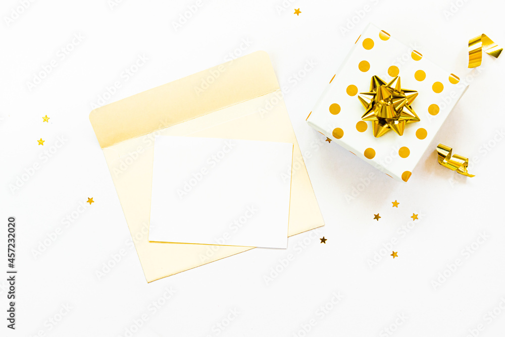 Top view of golden dotted gift box and an open envelope with empty card on a white background. Copy space, mock-up.