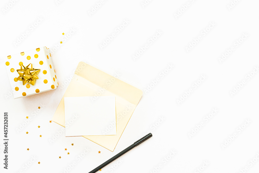Top view of golden dotted gift box and an open envelope with empty card on a white background. Copy space, mock-up.