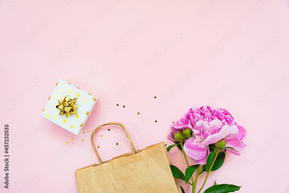 Flat lay of a gift box, a shopping bag and a peony flower over pink background. Copy space.