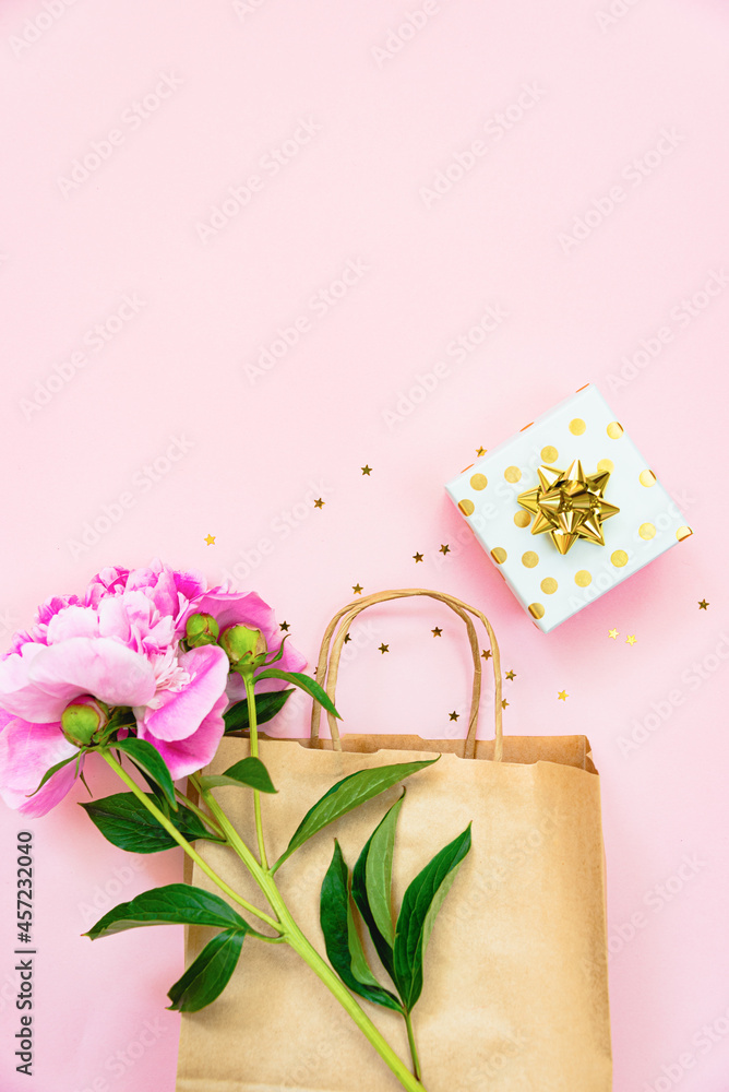 Flat lay of a gift box, a shopping bag and a peony flower over pink background. Copy space.