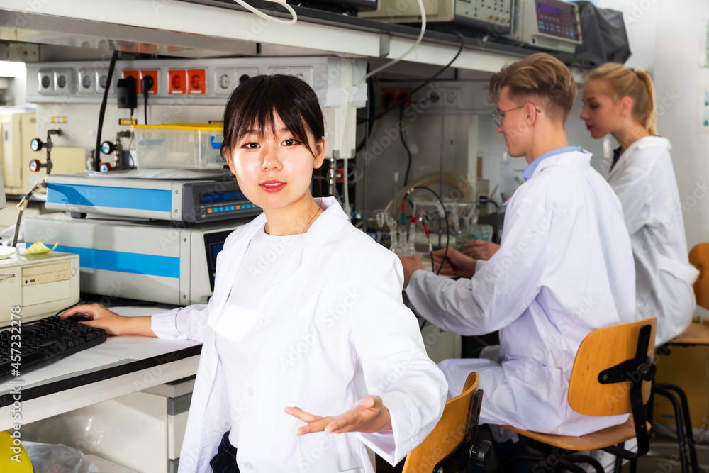 Portrait of positive Chinese woman lab technician engaged in research in chemical laboratory with her colleagues